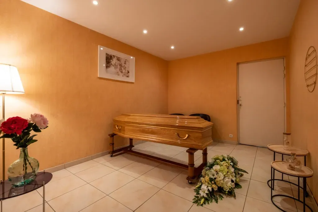 Chambre funéraire chaleureuse accueillant un cercueil et des compositions florales.