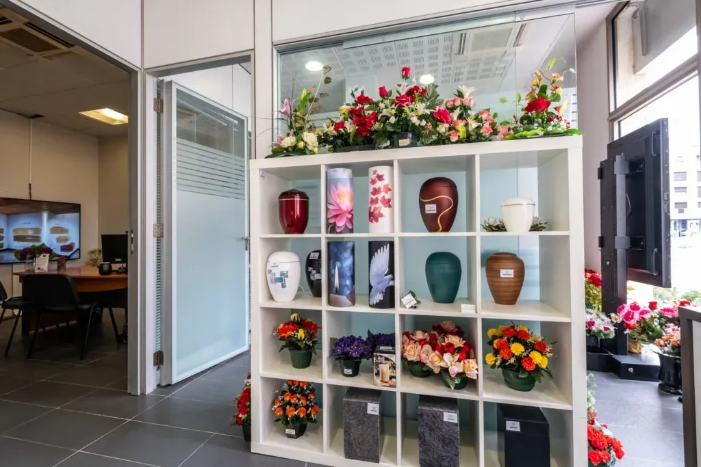 Étagère de présentation d'urnes funéraires et de fleurs artificielles dans la boutique.