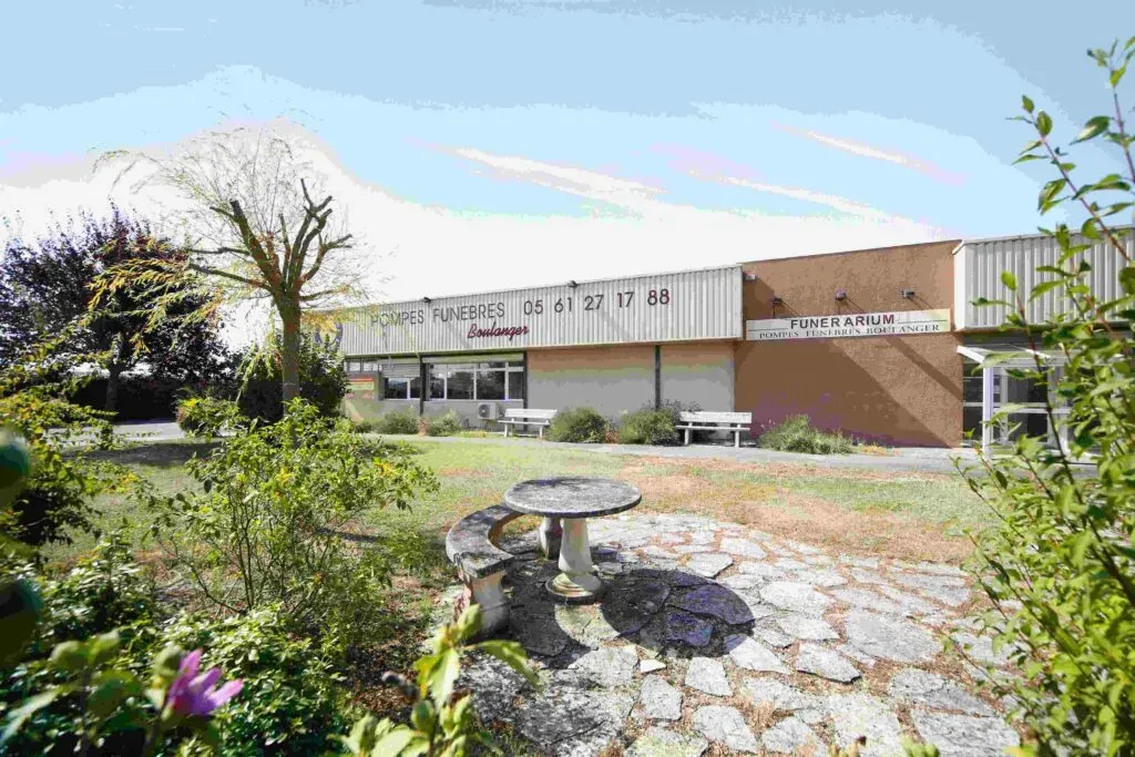 Façade extérieure du funérarium et des pompes funèbres avec espace vert et table en pierre.